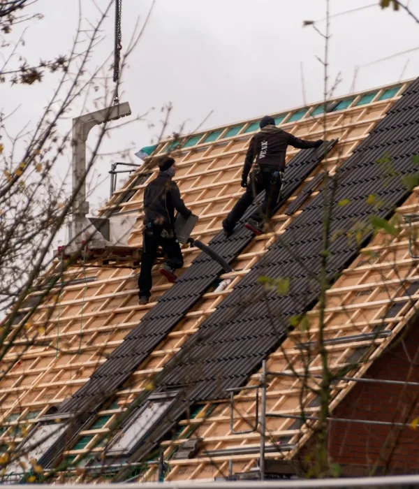Roofers installing shingles on a steep residential roof